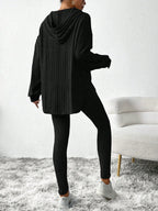 Back view of a woman wearing a black ribbed knit loungewear set with a hooded tunic and leggings.