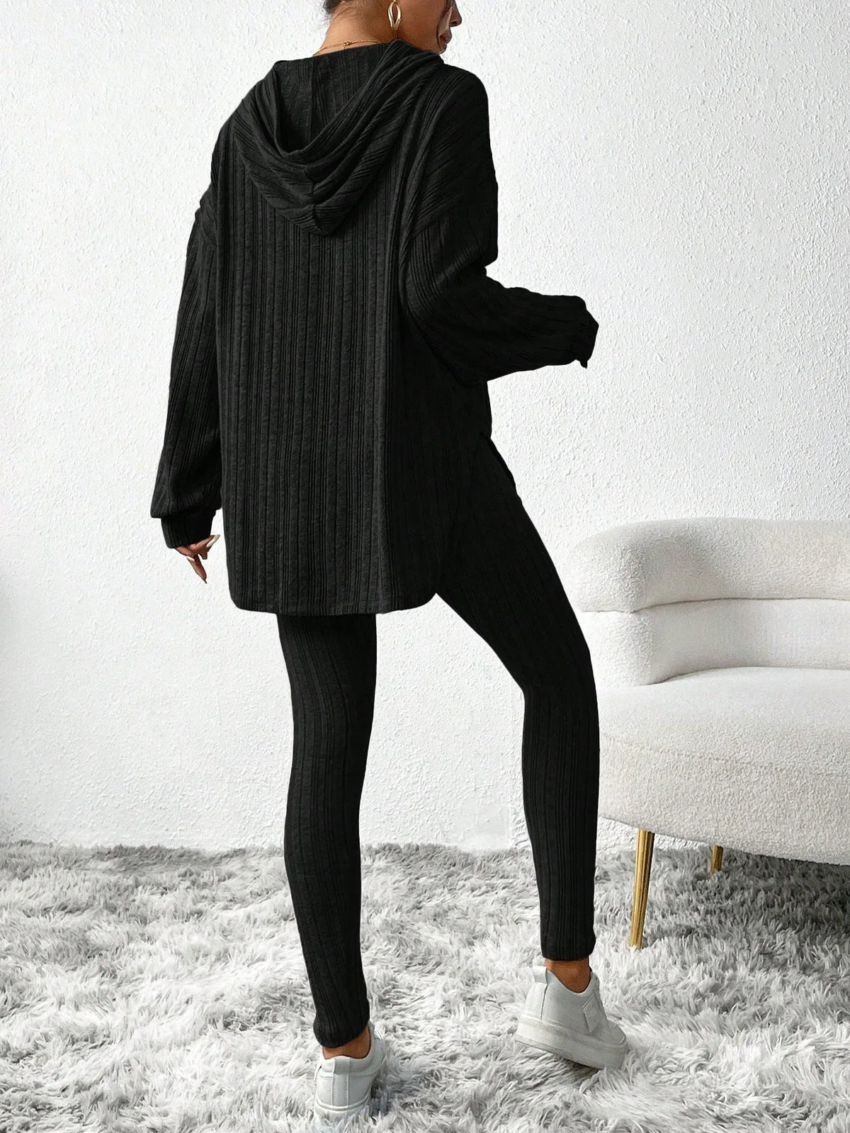 Back view of a woman wearing a black ribbed knit loungewear set with a hooded tunic and leggings.