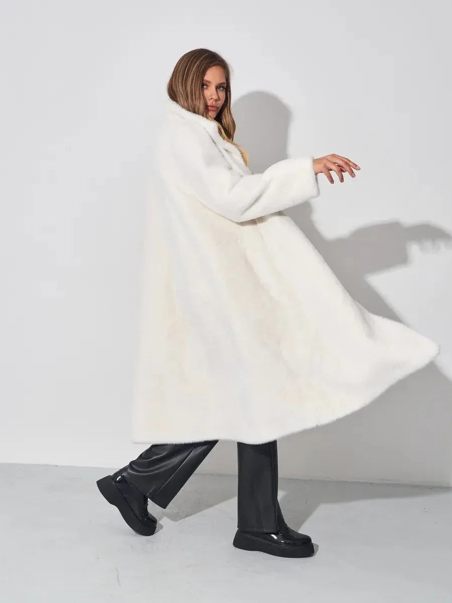 Woman in a white faux fur coat and black pants twirling against a white wall.