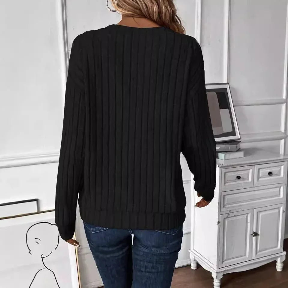 Back view of a woman wearing a black ribbed V-neck long-sleeve sweater with dark wash jeans.