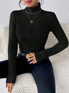 Woman wearing a black ribbed turtleneck sweater and black jeans, accessorized with gold necklaces and rings.