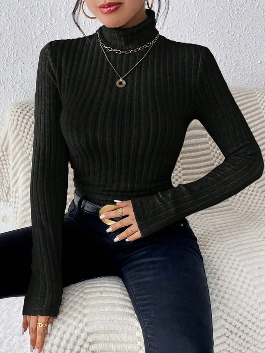 Woman wearing a black ribbed turtleneck sweater and black jeans, accessorized with gold necklaces and rings.
