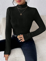 Woman wearing a black ribbed turtleneck sweater and black jeans, accessorized with gold necklaces and rings.