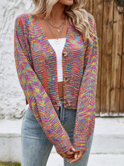 Woman wearing a multicolor rainbow knit cropped cardigan with a white top and blue jeans, standing outdoors.