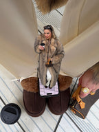 Street style shot of a woman in a warm, oversized faux fur coat against an architectural background.