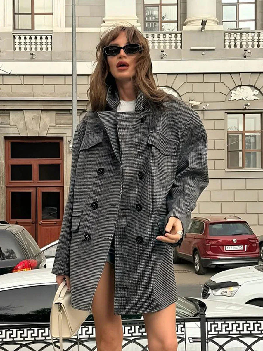 Woman wearing an oversized grey plaid double-breasted blazer with notched lapels and flap pockets, paired with a white t-shirt and shorts. Main image