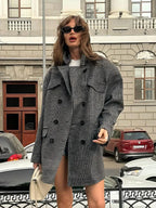 Woman wearing an oversized grey plaid double-breasted blazer with notched lapels and flap pockets, paired with a white t-shirt and shorts.