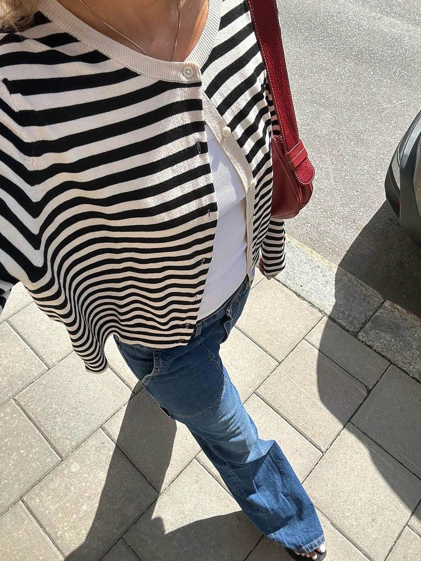 Top-down view of a woman's outfit featuring a black and white striped cardigan, white tank top, and blue jeans.