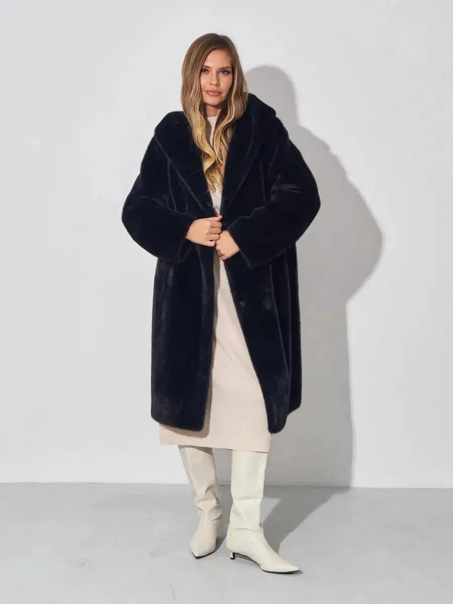 Woman wearing a black hooded faux fur coat, cream dress, and white boots, opening coat, front view.