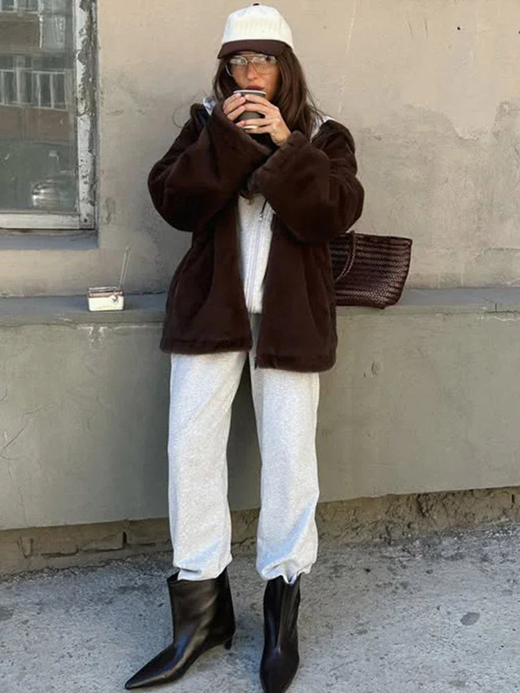 Woman wearing a brown faux fur hooded jacket over a grey hoodie and sweatpants, holding a coffee cup. Main image