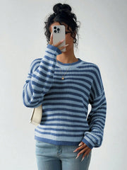 Woman wearing a blue and light blue striped knit sweater and light wash jeans, holding a smartphone up to her face.