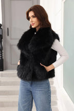 Woman wearing a black faux fur vest over a white long-sleeved shirt and blue jeans, with one hand on hip