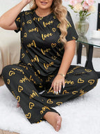 Woman wearing a black and gold "love" and heart print pajama set sitting cross-legged on a rug.