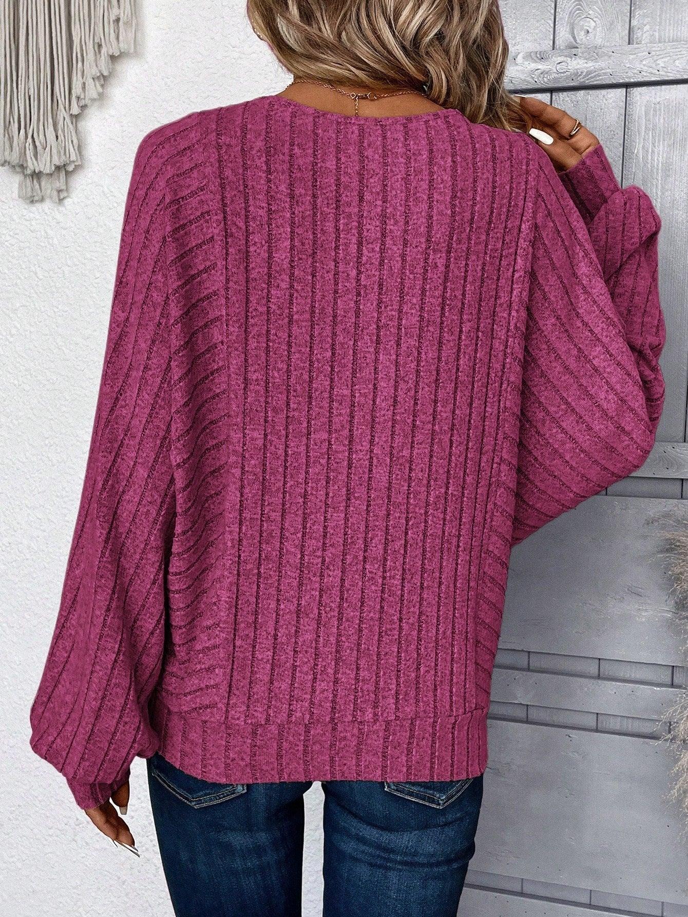 Back view of a woman wearing a magenta ribbed knit sweater with batwing sleeves and blue jeans.
