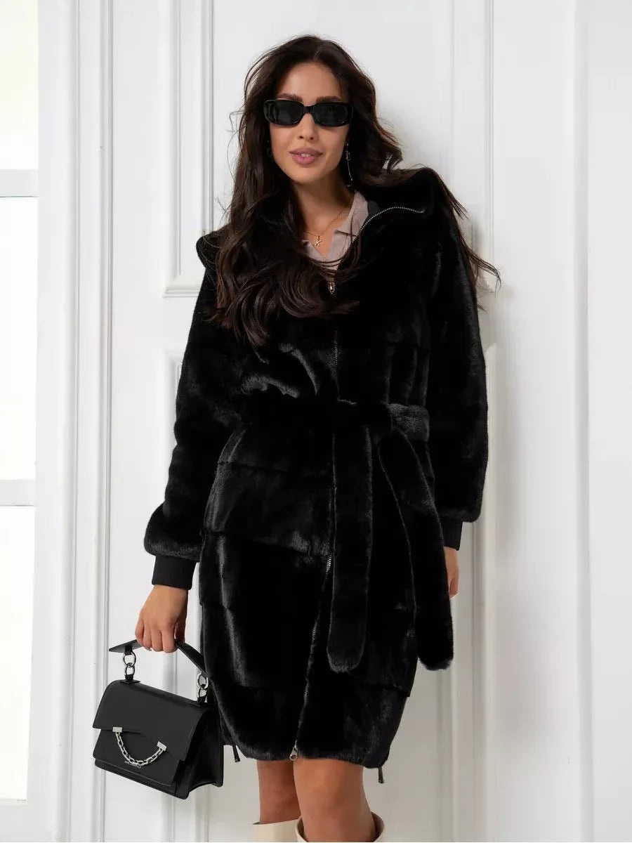Woman wearing a black hooded faux fur midi coat with a belted waist and zipper details, holding a black handbag.