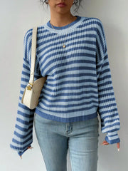 Close-up of a woman wearing a blue and light blue striped knit sweater, light wash jeans, and a cream shoulder bag.