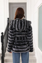 Back view of a woman wearing a hooded faux fur jacket with horizontal black and grey stripes and a belted waist.