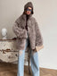 Woman wearing a gray curly faux shearling coat with a brown beanie and ripped blue jeans, holding a beige clutch bag.