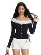 Model wearing a black off-the-shoulder long-sleeved top with white ruffled trim and white shorts, winking and touching her hair.
