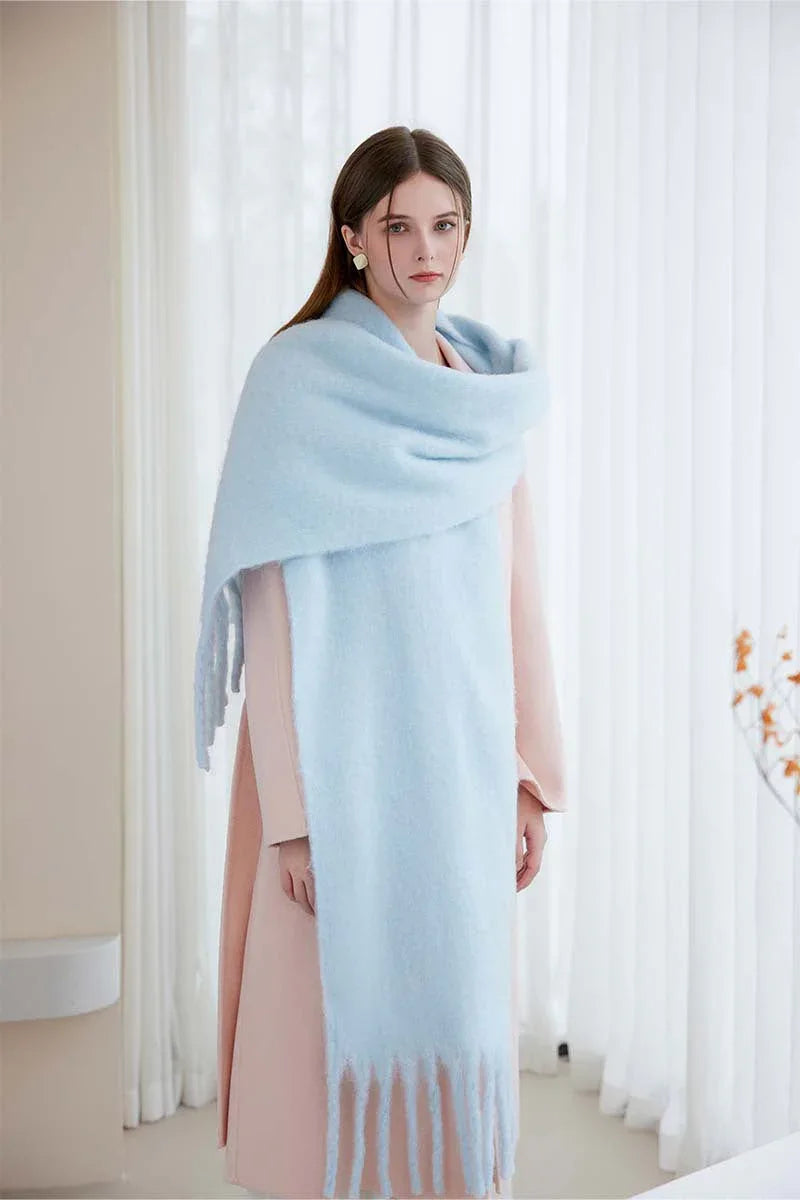 Woman wearing a light blue oversized mohair blend scarf with fringe, standing against a white background.