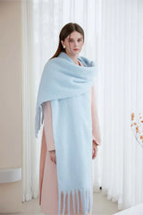 Woman wearing a light blue oversized mohair blend scarf with fringe, standing against a white background.