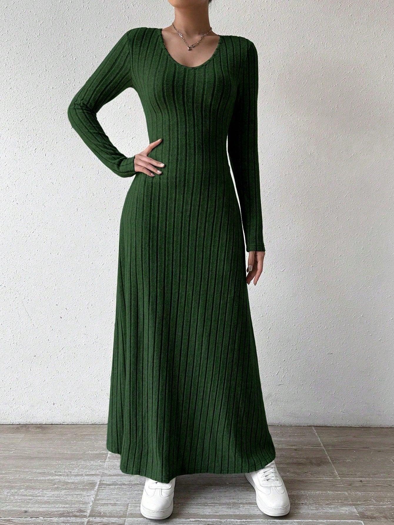 Woman wearing a long-sleeved green ribbed maxi dress, with one hand on her hip, wearing white sneakers, posing against a white wall.