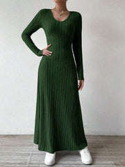 Woman wearing a long-sleeved green ribbed maxi dress, with one hand on her hip, wearing white sneakers, posing against a white wall.