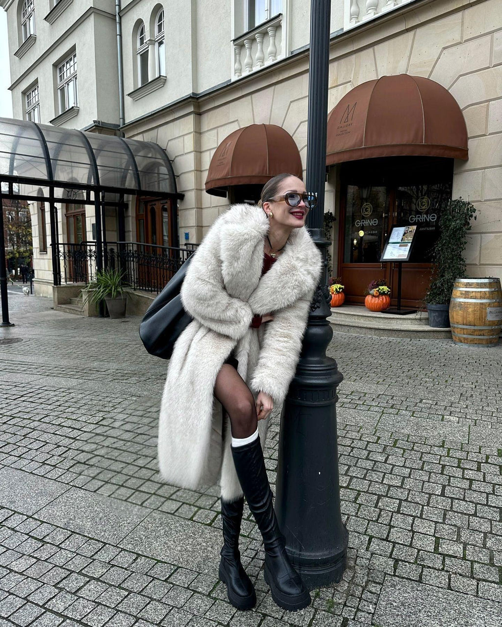 Woman leaning on a lamppost in a white faux fur coat
