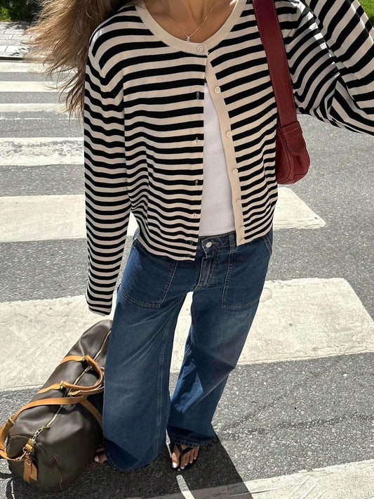 Close-up of a woman wearing a black and white striped cardigan, white tank top, and wide-leg blue jeans, with a red shoulder bag.