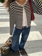 Close-up of a woman wearing a black and white striped cardigan, white tank top, and wide-leg blue jeans, with a red shoulder bag.