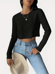 Woman wearing a black ribbed long-sleeve cropped top and light wash high-waisted jeans, holding a light-colored hat.
