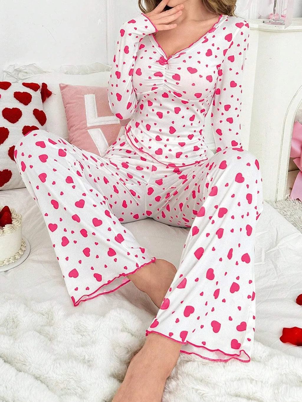 woman wearing white and pink heart print pajama set, seated on bed, facing forward