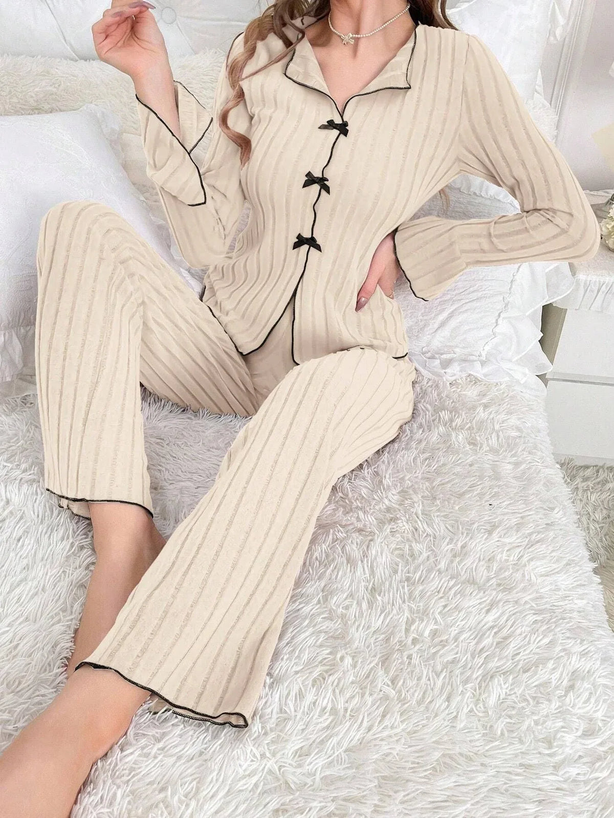 woman sitting on a bed in cream ribbed knit pajama set with black trim