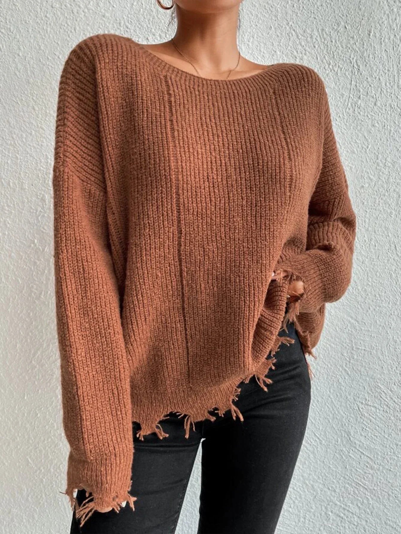 Woman wearing a rust-colored oversized distressed knit sweater with black pants and a necklace