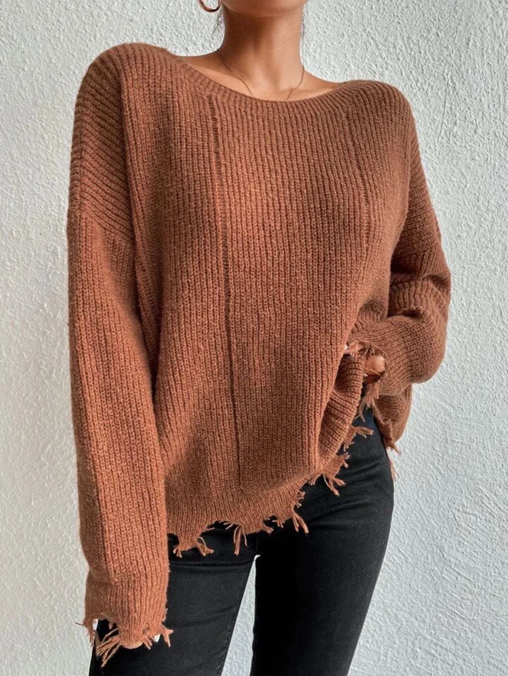 Woman wearing a rust-colored oversized distressed knit sweater with black pants and a necklace