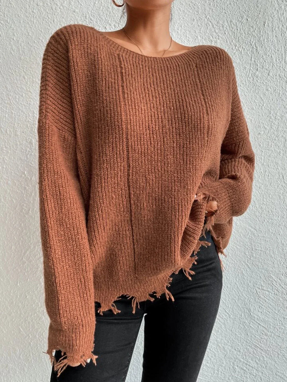 Woman wearing a rust-colored oversized distressed knit sweater with black pants and a necklace