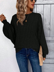 Woman wearing a black ribbed knit sweater, blue jeans, and sunglasses, holding a tan clutch.