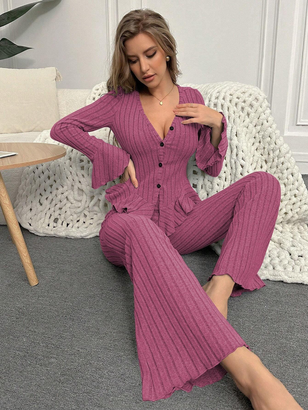 Woman sitting on the floor in a pink ribbed knit loungewear set, posing with her hand on her chest.