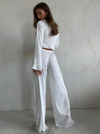 Rear view of a woman wearing a white sheer knit crop top and wide-leg pants.
