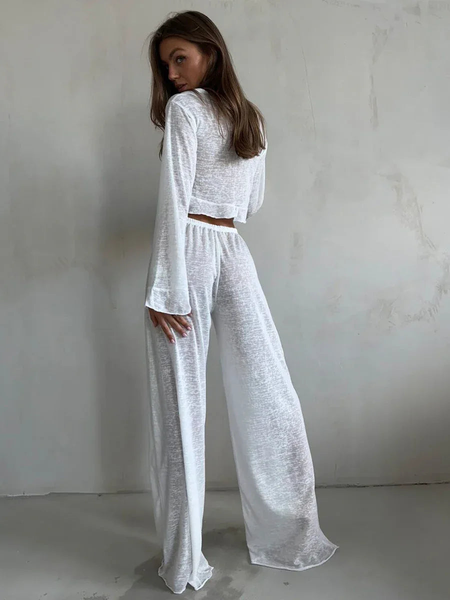 Rear view of a woman wearing a white sheer knit crop top and wide-leg pants.