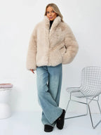Woman standing wearing a beige faux fur jacket and blue jeans