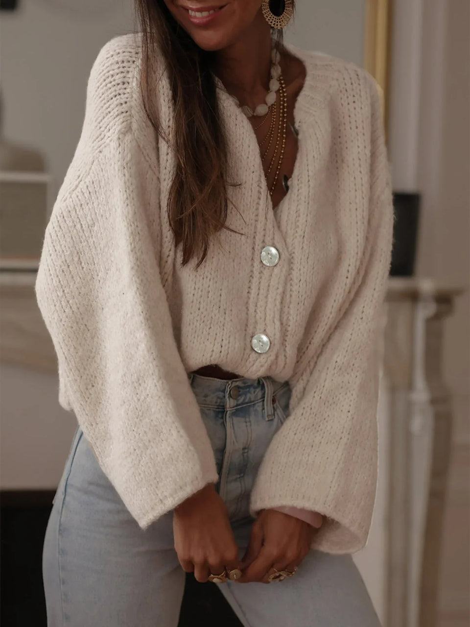 Model wearing a cream oversized chunky knit cardigan with balloon sleeves and v-neck, paired with light wash denim jeans. Main image