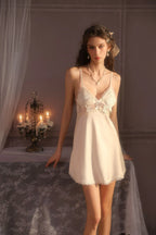 Woman wearing a white satin babydoll nightgown with lace trim and a matching robe, standing next to a table with candles.