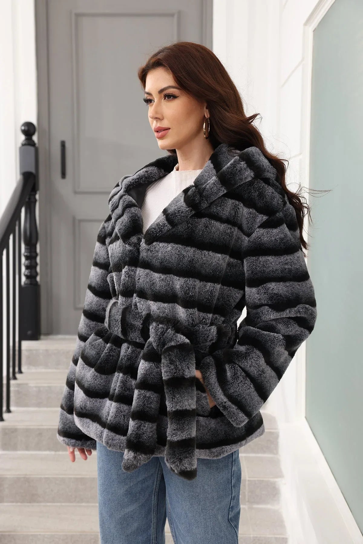 Woman in a hooded faux fur jacket with horizontal stripes, shown from the side.