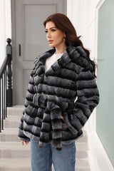 Woman in a hooded faux fur jacket with horizontal stripes, shown from the side.