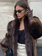 woman adjusting her sunglasses while wearing a stylish brown fur coat and leather gloves