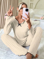 Woman taking a selfie while sitting on the floor in a cream ribbed knit pajama set with black trim.