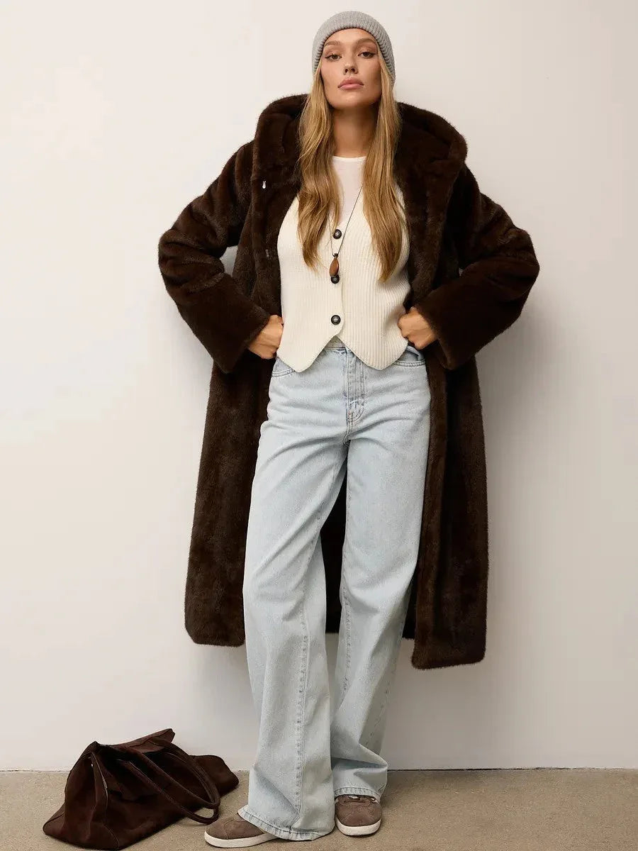 Woman wearing a brown hooded faux fur coat, white top, light wash jeans, and a grey beanie, with hands on hips.