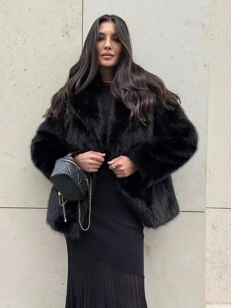 Woman wearing a black faux fur jacket over a black dress and holding a black purse.
