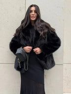 Woman wearing a black faux fur jacket over a black dress and holding a black purse.